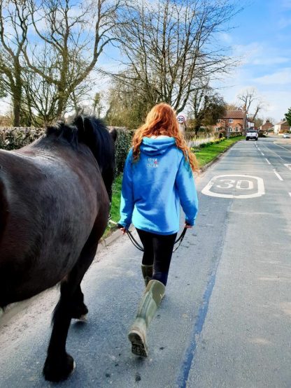 Girl in blue eventing hoodie walking her horse